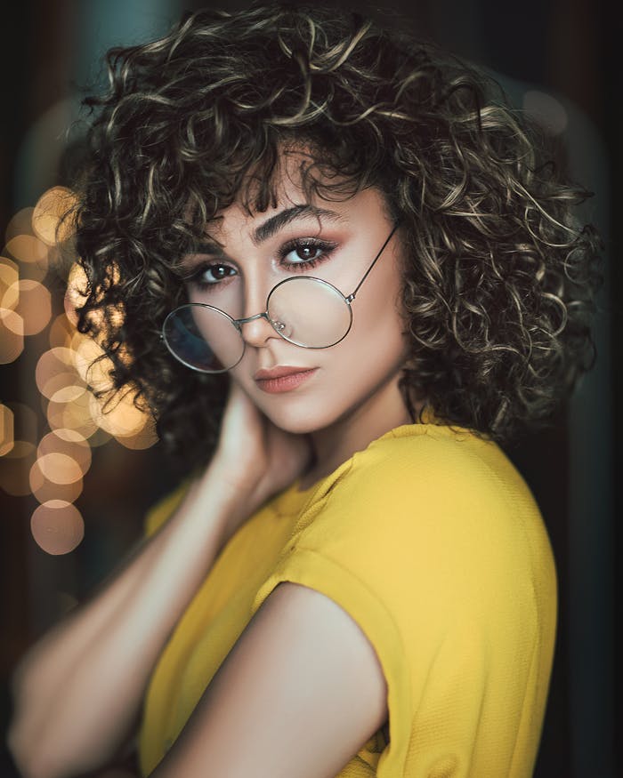 Stylish portrait of a woman with curly hair and eyeglasses in a vibrant setting.